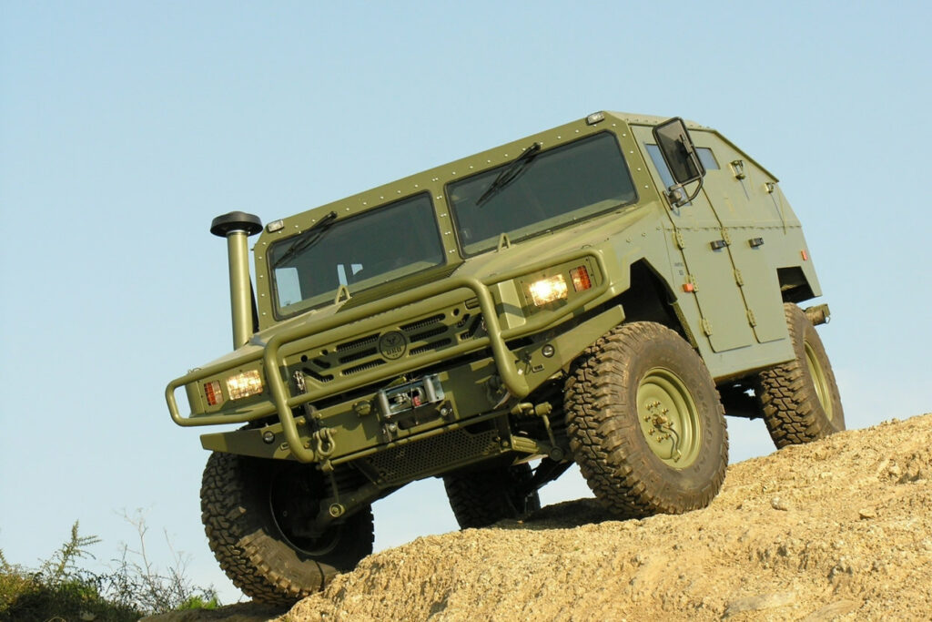 An armoured dark green coloured hummer parked on top of a hill